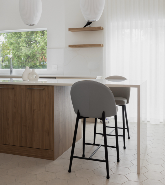 Îlot moderne avec armoires de cuisine en bois et comptoir blanc, accompagné de tabourets élégants, dans une cuisine lumineuse au design minimaliste.