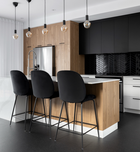 Cuisine moderne avec armoires en bois et noires, îlot central avec comptoir blanc, et suspensions industrielles, créant un espace élégant et contemporain.