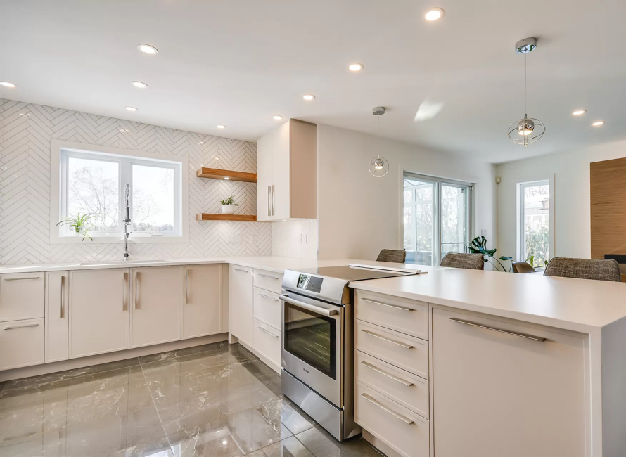 Cuisine lumineuse avec armoires blanches, dosseret en chevron et îlot spacieux, offrant un design moderne et épuré pour un espace fonctionnel et élégant.