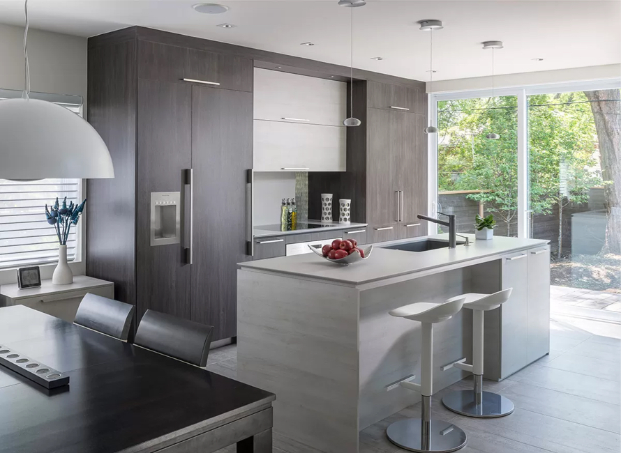 Cuisine moderne avec armoires en mélamine effet bois foncé, îlot central aux lignes épurées et espace lumineux grâce aux grandes baies vitrées, créant un design élégant et fonctionnel.