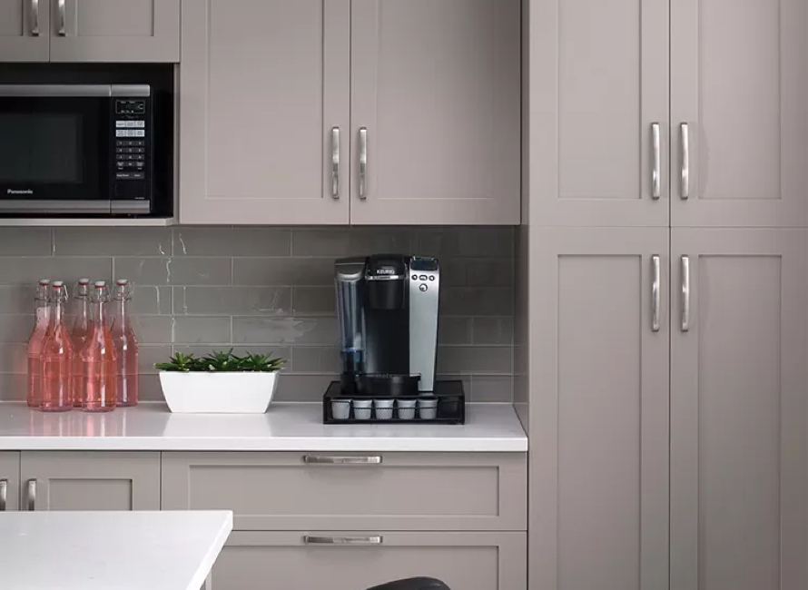 Cuisine élégante avec armoires en MDF gris, comptoir en quartz blanc et dosseret en carrelage brillant, offrant un espace fonctionnel avec un coin café moderne.