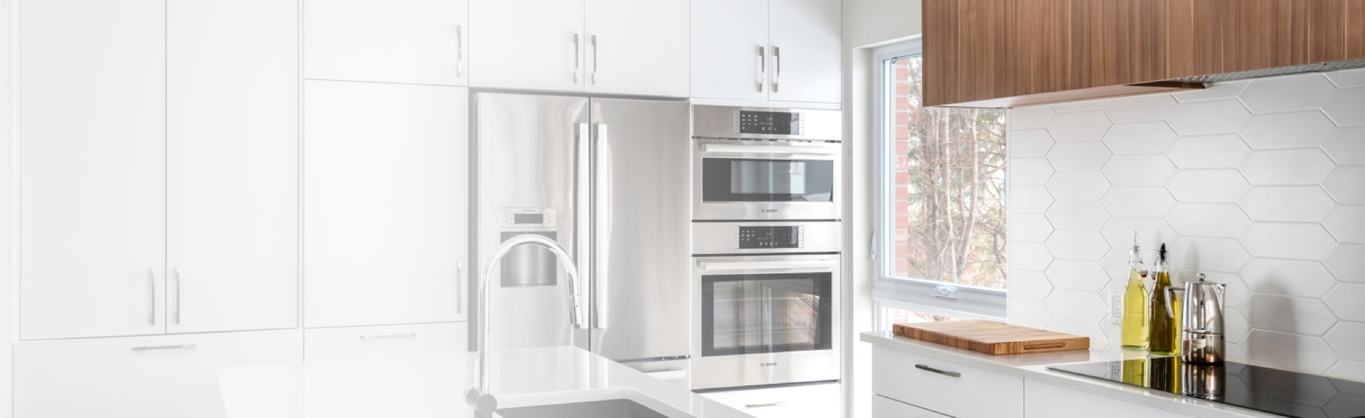 Cuisine moderne avec îlot central en quartz, meubles gris élégants et réfrigérateur encastré. Grand espace lumineux avec vue sur l’extérieur, créant une ambiance contemporaine et fonctionnelle.