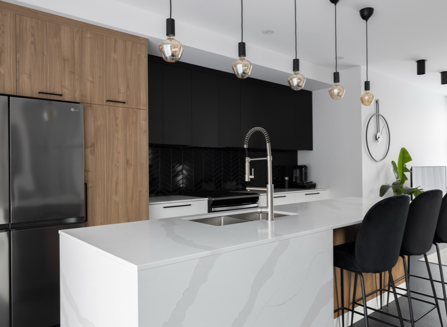 Comptoir de cuisine en quartz effet marbre avec îlot central, associé à des armoires en bois et noires pour un design moderne et raffiné. Éclairage suspendu et tabourets élégants complètent l’ensemble.