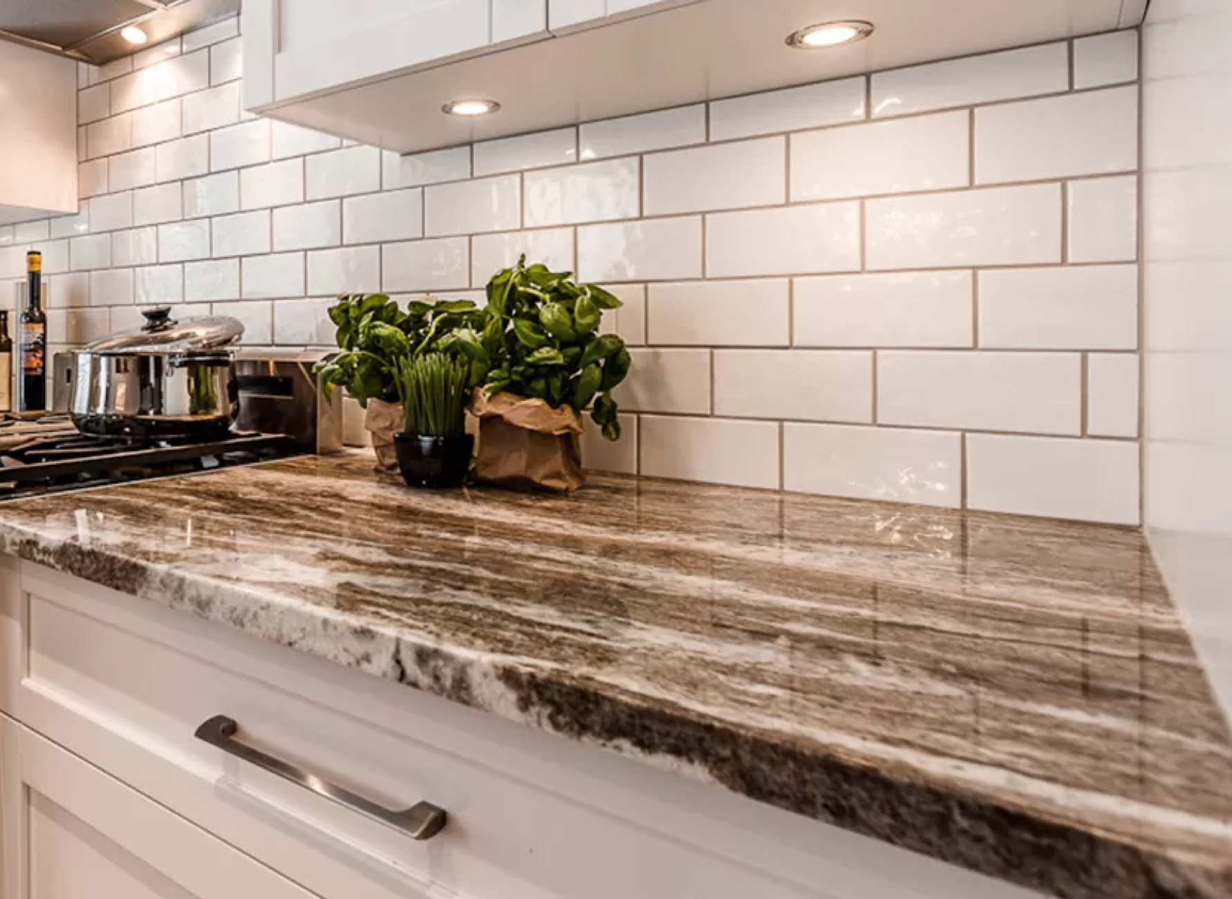 Comptoir de cuisine en granit poli aux nuances naturelles, accompagné d’une crédence en carrelage métro blanc. Un design élégant alliant robustesse et modernité.
