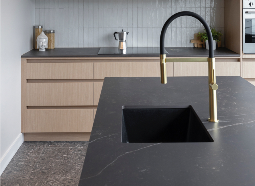 Comptoir de cuisine en Dekton noir mat avec évier intégré et robinet doré au design contemporain. Assorti à des armoires en bois clair et une crédence en carrelage texturé pour une finition élégante et moderne.
