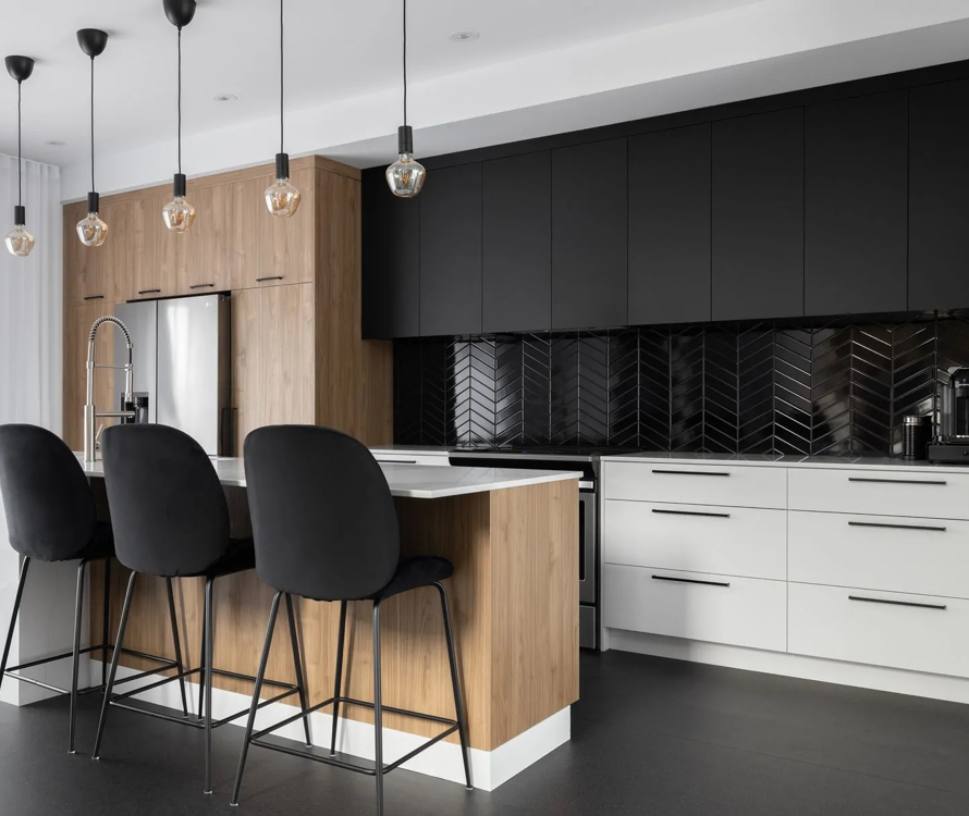 Modern kitchen with a sleek design featuring a central wood island, black chairs, and stylish pendant lights. Contrasting black and white cabinetry with a black chevron tile backsplash adds a refined contemporary touch.