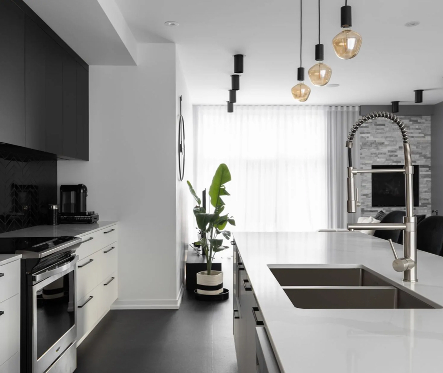 Open modern kitchen with a central island and a double stainless steel sink, illuminated by designer pendant lights. A bright space with large windows and a view of the contemporary-style living room.
