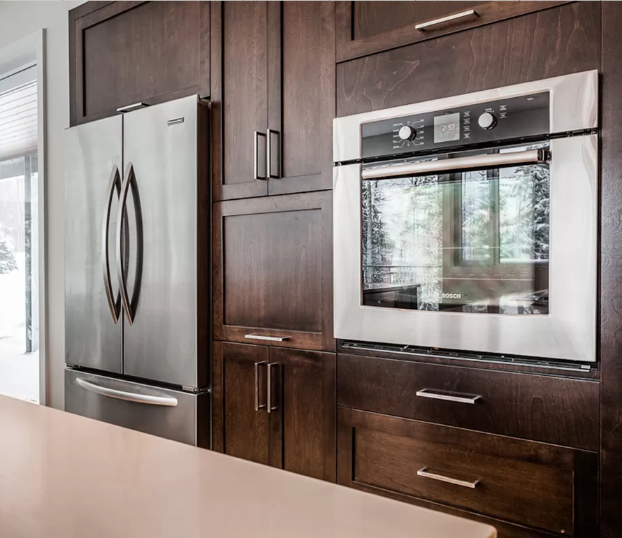 Modern kitchen with stainless steel appliances integrated into dark wood cabinetry. A built-in oven and French door refrigerator provide an elegant and functional design.