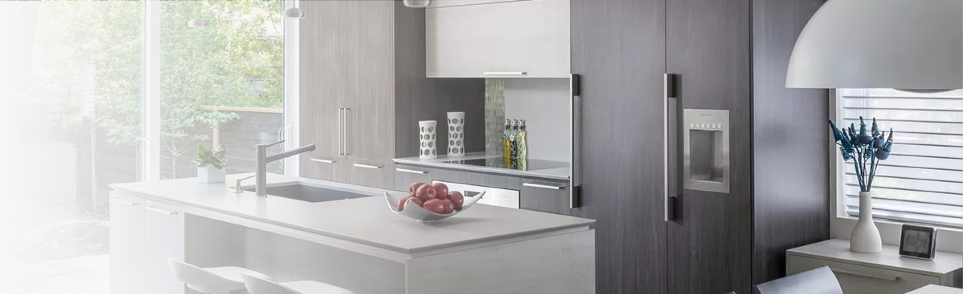 Modern kitchen with a central quartz island, elegant gray cabinetry, and a built-in refrigerator. A spacious, bright area with a view of the outdoors, creating a contemporary and functional ambiance.
