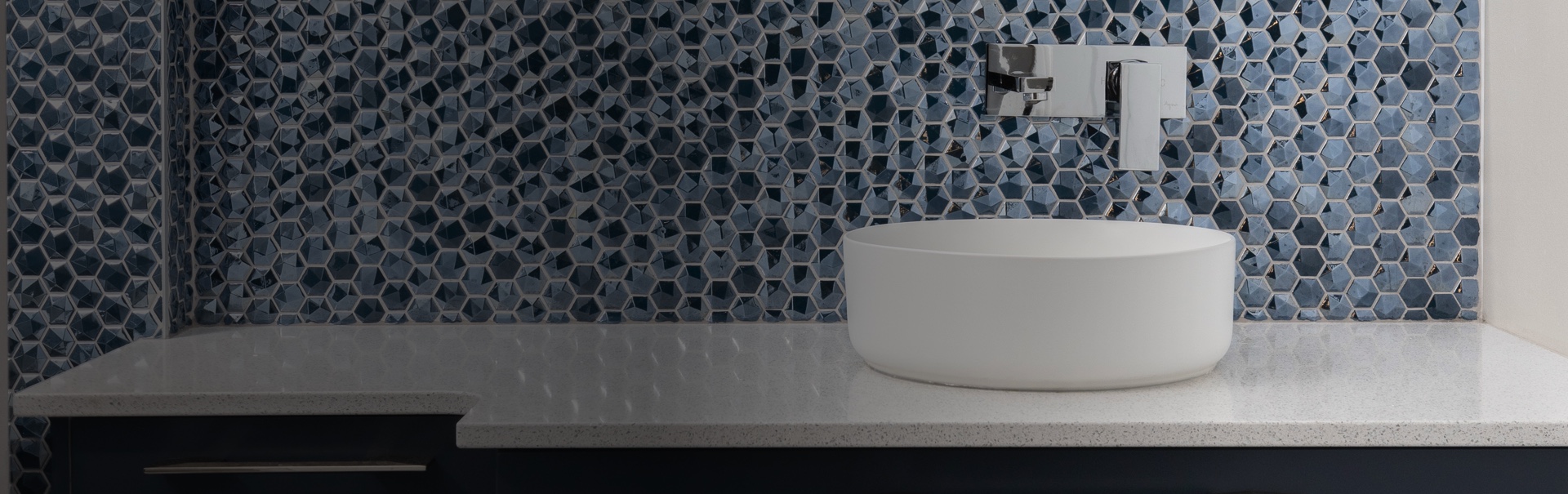 Vasque design sur plan en quartz blanc avec crédence en mosaïque bleue hexagonale, illustrant l’élégance des salles de bain sur mesure.