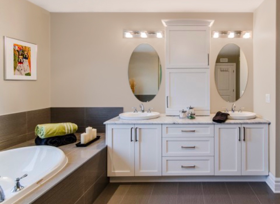 Double vasque encastrée avec rangements blancs, miroir ovale et baignoire d’angle, illustrant une salle de bain sur mesure au style classique et chaleureux.