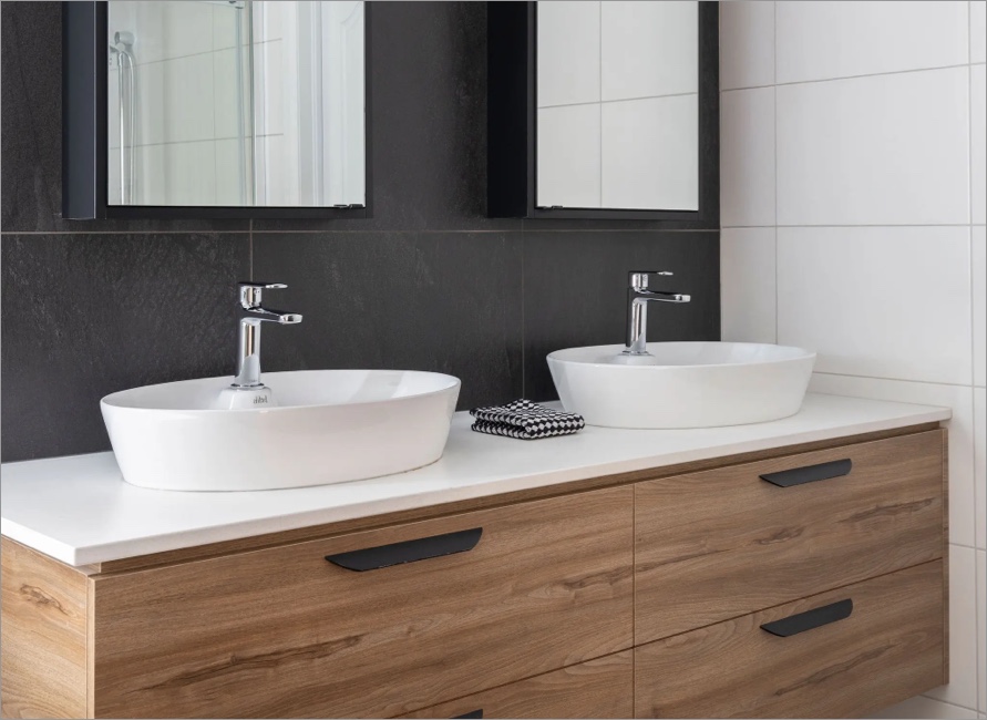 Meuble en bois clair avec double vasque blanche et mur contrastant noir, exemple de salle de bain sur mesure au style contemporain.